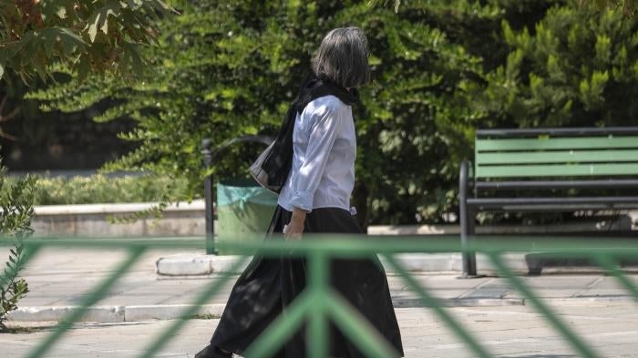 An elderly Iranian woman walks along a street-side in Tehran without wearing her headscarf.