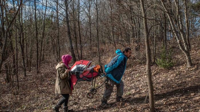 A man and his daughter carry a baby in a stroller through a forest