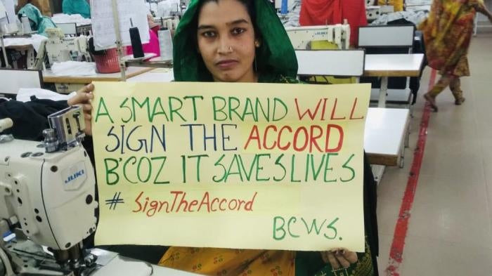 A garment factory worker in Bangladesh holds a sign to stand up for safe factories and the International Health and Safety Accord