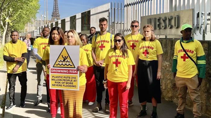 Campaigners and waste pickers from around the world holding a sign reading, “plastic puts 218 million people at risk of more severe flooding,” outside the UNESCO Headquarters in Paris, where the second round of plastics treaty negotiations took place, May 30, 2023.