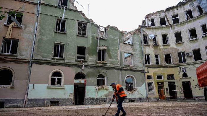 A communal worker sweeps outside an apartment building in Lviv, Ukraine, on July 7, 2023, a day after it was seriously damaged by a Russian missile strike. 