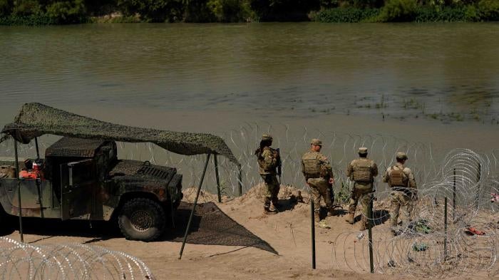 Guardsmen stand by a river lined with razorwire