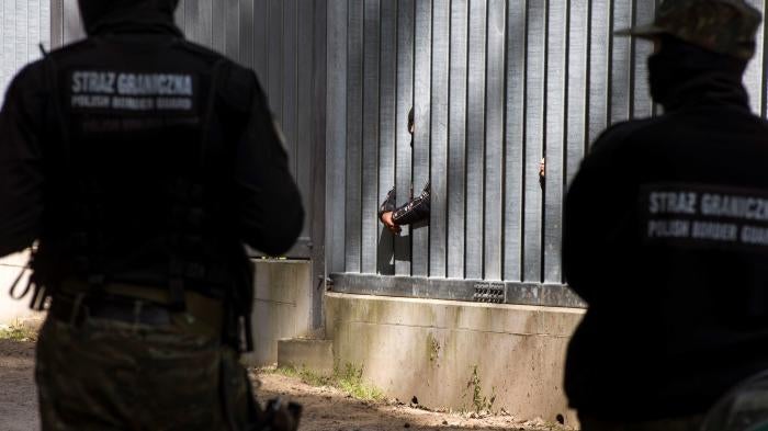 border guards watch asylum seekers stuck behind a border wall 