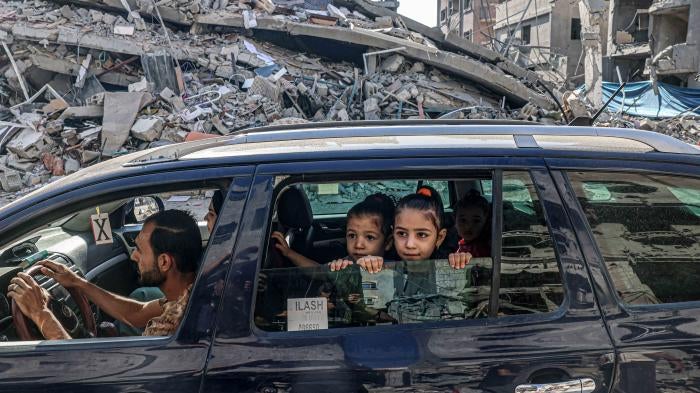A family in a car drives passed destroyed buildings