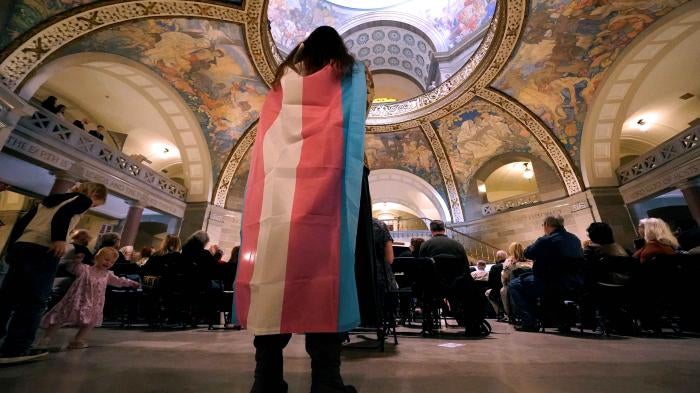 Glenda Starke wears a transgender flag as a counter protest during a rally in favor of a ban on gender-affirming health care legislation, March 20, 2023, at the Missouri Statehouse in Jefferson City. ©2023 AP Photo/Charlie Riedel, File