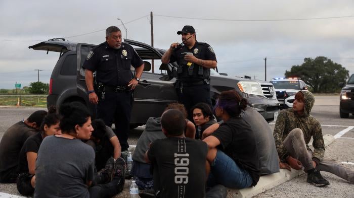 Asylum seekers from Central America sit by the road after police detained them in Hondo, Texas, about 100 miles from the US-Mexico border, June 1, 2022. 