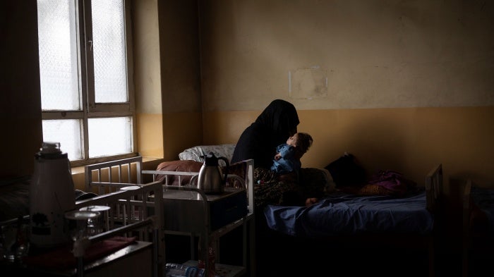 An unidentifiable woman holds her baby son on a hospital bed