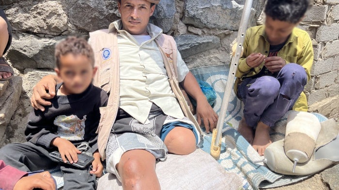عبد الله (35 عاما) خسر ساقيه جراء لغم أرضي بينما كان يأخذ الماعز للرعي، يجلس على الأرض مع طفليه في الشقب، اليمن في 27 أبريل/نيسان 2024. © 2024 نيكو جعفرنيا/هيومن رايتس ووتش