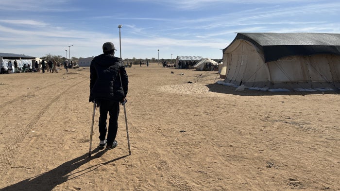 A man stands on crutches in a refugee camp