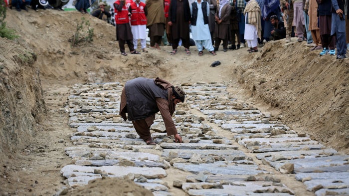 A man places stones on graves during a mass funeral for victims of the Pakistani  airstrike on the Omid drug rehabilitation center in Kabul, Afghanistan