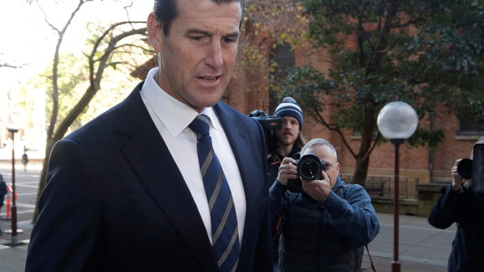a man arrives at a courthouse followed by reporters