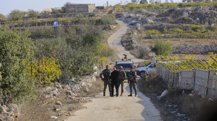 Palestinians stand behind a barrier as Israeli forces block farmers from accessing their lands in Halhul town near Hebron, in the occupied West Bank, on November 20, 2025.