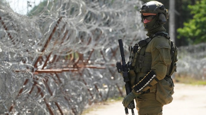 A Polish border guard stands near a barbed wire fence at the Polish-Belarusian border in Polowce, Poland, July 21, 2025. © 2025 AP Photo/Czarek Sokolowski