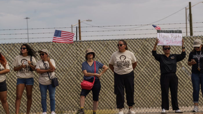 Protesters opposing mass deportations by ICE hold signs during a demonstration held outside of Fort Bliss