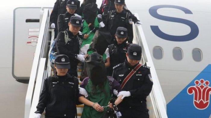 Police escort a group of people deported from Kenya as they get off a plane at Beijing Capital International Airport on April 13, 2016.