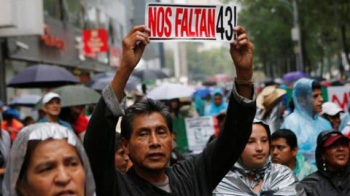 A protester holds up a sign next to relatives of some of the 43 missing students of Ayotzinapa College Raul Isidro Burgos during a march in Mexico City