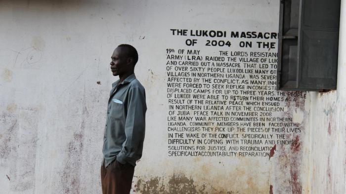 A community member in Lukodi stands next to a memorial of a May 19, 2004 massacre, one of the atrocities for which Dominic Ongwen is facing charges before the International Criminal Court. Over 4,000 victims are participating in the trial. ©2016 G. GT.