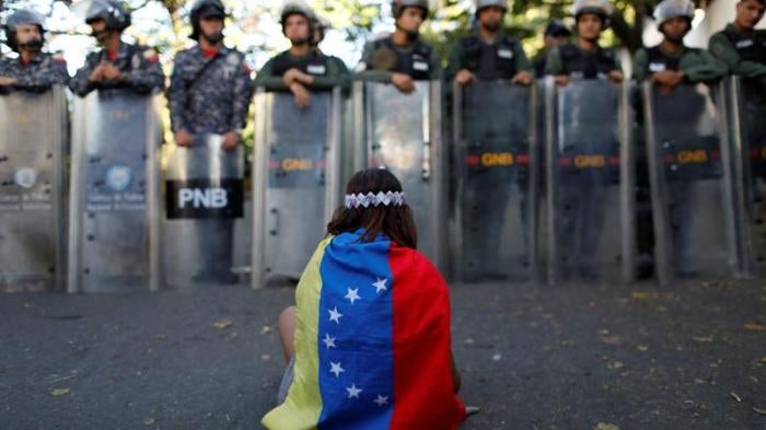 A girl wears a Venezuelan flag as Venezuelan security forces block access to opposition supporters and mourners of rogue ex-policeman Oscar Perez to the main morgue of the city, in Caracas, Venezuela January 20, 2018. 