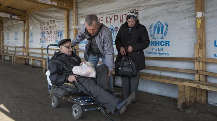 An older man with a disability sits on an old luggage cart preparing to cross the Stanitsa Luhanska border point in Eastern Ukraine. 