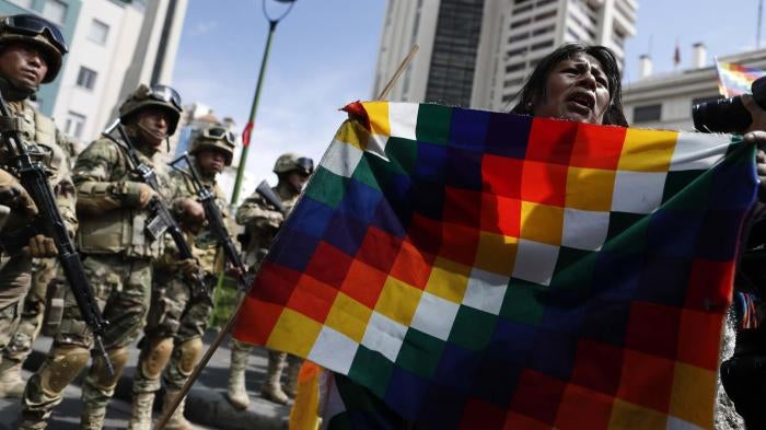 A demonstrator holds a Wiphala flag in front of soldiers blocking a street in downtown La Paz, Bolivia, Friday, Nov. 15, 2019.