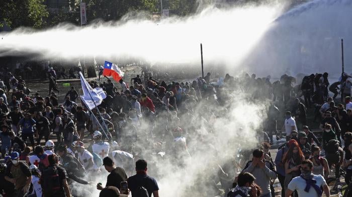 Demonstrators run from police launching water canons and tear gas as a state of emergency remains in effect in Santiago, Chile, Sunday, Oct. 20, 2019. 