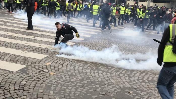 Protester picks up a tear gas grenade during a police charge on December 8, 2019 on the Champs Elysees, Paris.