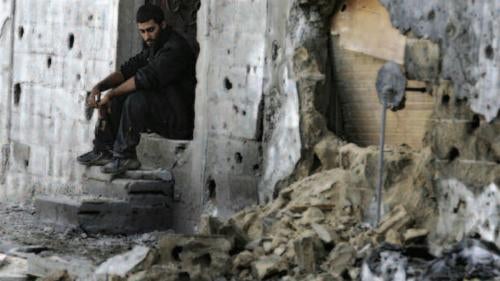 A Palestinian man sits in front of his damaged home after Israeli artillery fired on Beit Hanoun on November 8, 2006. The attack killed 23 Palestinian civilians and wounded at least 40 more. It led Israel to initiate a moratorium on artillery fire in Gaza, which continued at the time this report was printed. 