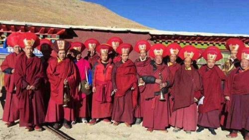 A row of monks in red outfits and headdresses pose for a photo