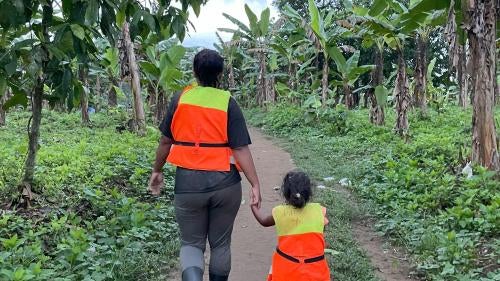 A Venezuelan woman, wearing a lifejacket, holds her daughter’s hand as they walk in a jungle