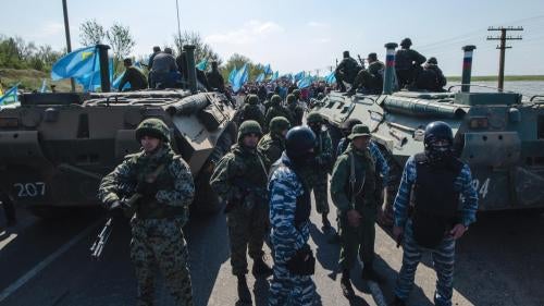 Army and police officers block the road ahead of a protest by Crimean Tatars (visible in the background) at a Russia-Ukraine border checkpoint outside the town of Armyansk, Crimea on May 3, 2014.