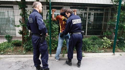 Police officers perform an identity check and body pat-down of a young man in Paris, France.
