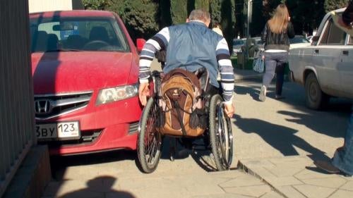 Alexander Simyonov navigates his wheelchair around a parked car in the Adler district of Sochi, February 8, 2013.