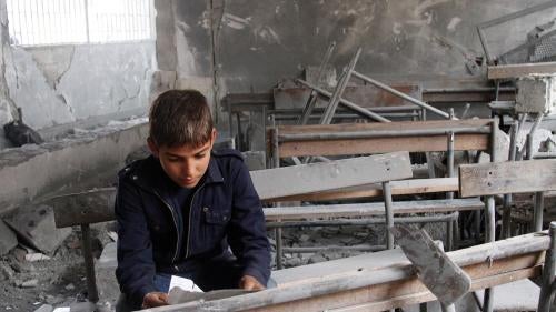 A boy sits inside his now-destroyed former classroom in Aleppo, Syria.