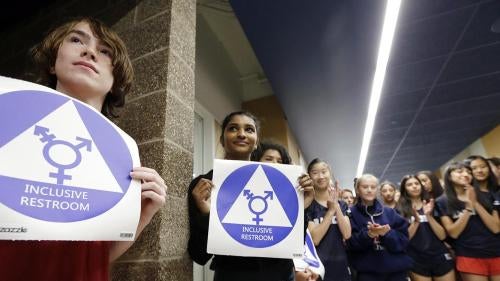 Students hold stickers about to be placed on a new all-gender bathroom as members of the cheer squad applaud at Nathan Hale High School in Seattle, WA on May 17, 2016. 
