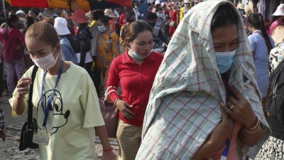 In this March 20, 2020, photo, garment factory workers wear face masks as they walk out at the end of their work shift near Phnom Penh, Cambodia. 