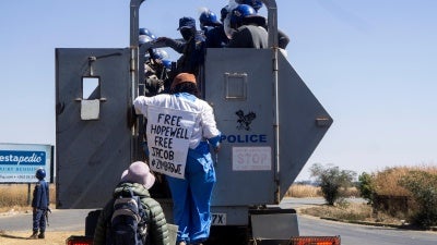 Zimbabwean novelist Tsitsi Dangarembga (center) and her colleague Julie Barnes hold placards as they are arrested during an anti-corruption protest march in Harare, Zimbabwe, on July 31, 2020.  © 2020 ZINYANGE AUNTONY / AFP