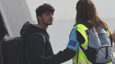 An officer from the European Union’s border protection agency, Frontex, holds the arm of a migrant as they board a ferry in the port of Mytilini, Lesbos island, Greece, on Friday, April 8, 2016.