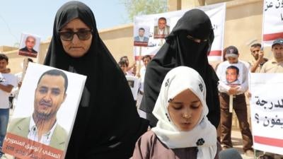 Tawfiq al-Mansouri's mother, daughter, and wife hold up a photo of him during a demonstration. Al-Mansouri is one of four imprisoned Yemeni journalists currently facing the death penalty.
