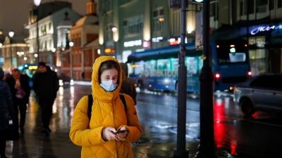 A woman wearing a face mask looks at her smartphone as she walks through a street in Moscow, Russia, November 23, 2020. 