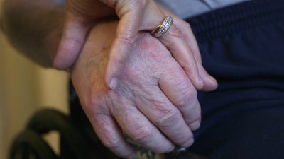 A nursing home resident holds his wife's hand.