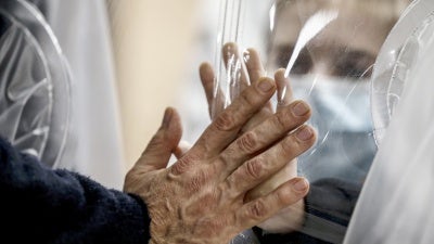 Relatives touch each other's hand through a plastic film screen and a glass to avoid contracting Covid-19 at the San Raffaele center in Rome, Italy, Dec. 22, 2020