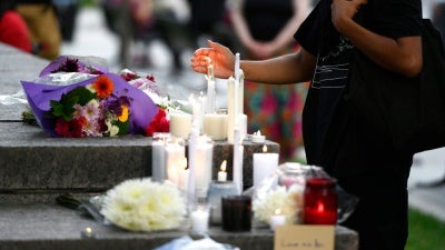 A mourner shields a candle from the wind after placing it at a memorial for the four family members who were killed in a vehicle attack in London, Ontario, in Ottawa, on Tuesday, June 8, 2021.