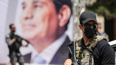 An Egyptian intelligence security detail member stands guard near a banner showing President Abdel Fattah al-Sisi.
