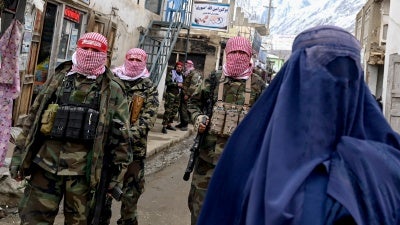 An Afghan woman walks by Taliban security personnel inalong a market in the Baharak district of Badakhshan province, February 26, 2024.