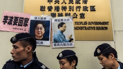 Police walk past missing person notices for Swedish publisher Gui Minhai (L) and Hong Kong publisher Yau Wentian, posted on the sign of China's Liaison Office in Hong Kong, January 3, 2016.