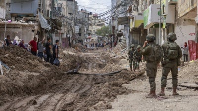 Israeli soldiers look on as Palestinian men and women carry their belongings on May 2, 2025 amid ongoing Israeli military operations and demolition of homes in Tulkarem refugee camp. Israeli forces had emptied the refugee camp of its inhabitants weeks prior.