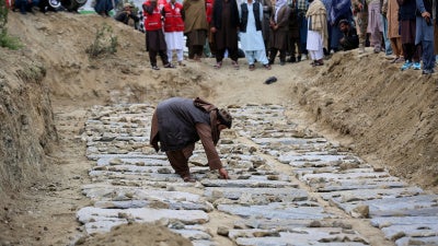 A man places stones on graves during a mass funeral for victims of the Pakistani  airstrike on the Omid drug rehabilitation center in Kabul, Afghanistan
