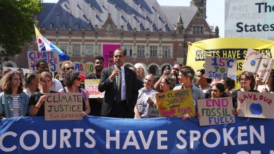 A man speaks during a demonstration with a banner that reads "Courts Have Spoken"