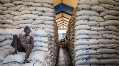 A worker sits atop sacks of food aid in a hangar where supplies are piling up because deliveries have halted because of the conflict at a World Food Programme (WFP) warehouse in Bor, Jonglei State, on February 13, 2026.