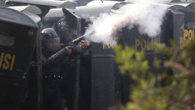 A police officer in protective gear fires tear gas